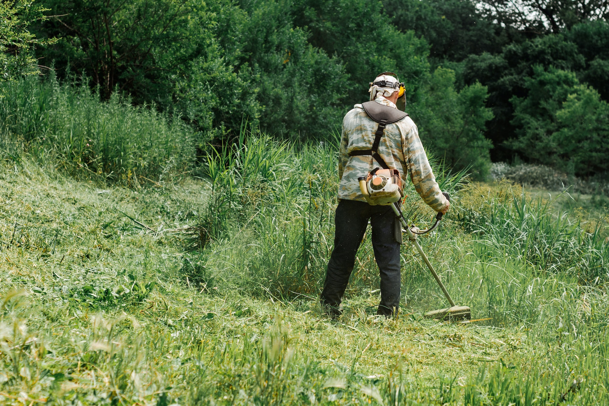 A working man mowing the tall grass with a lawn mower.