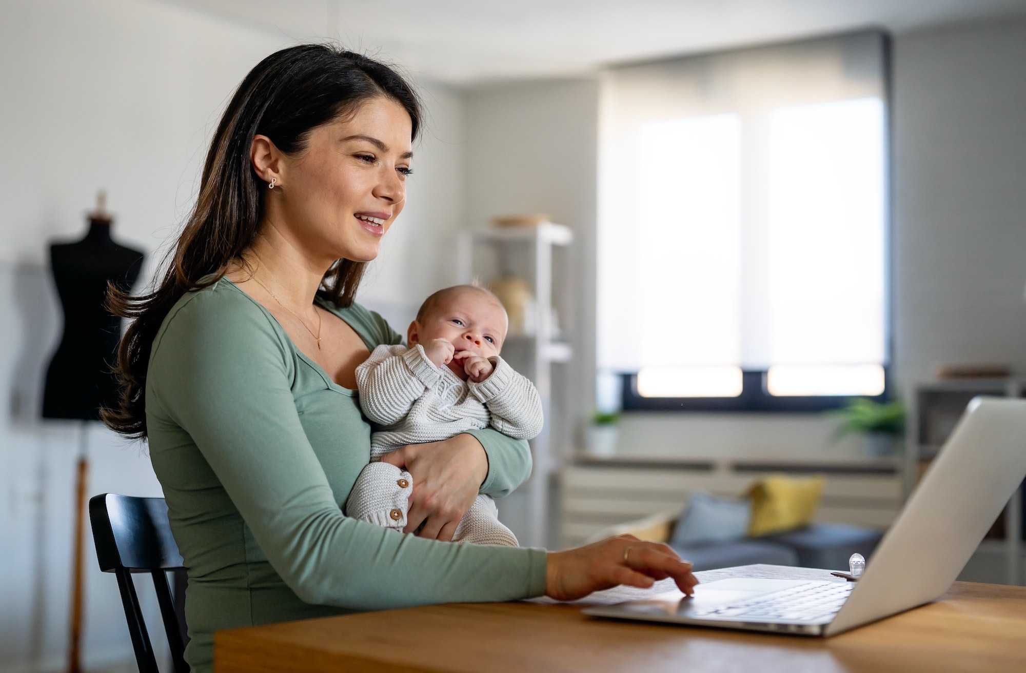 Stay at home mom working remotely on laptop while taking care of her baby.