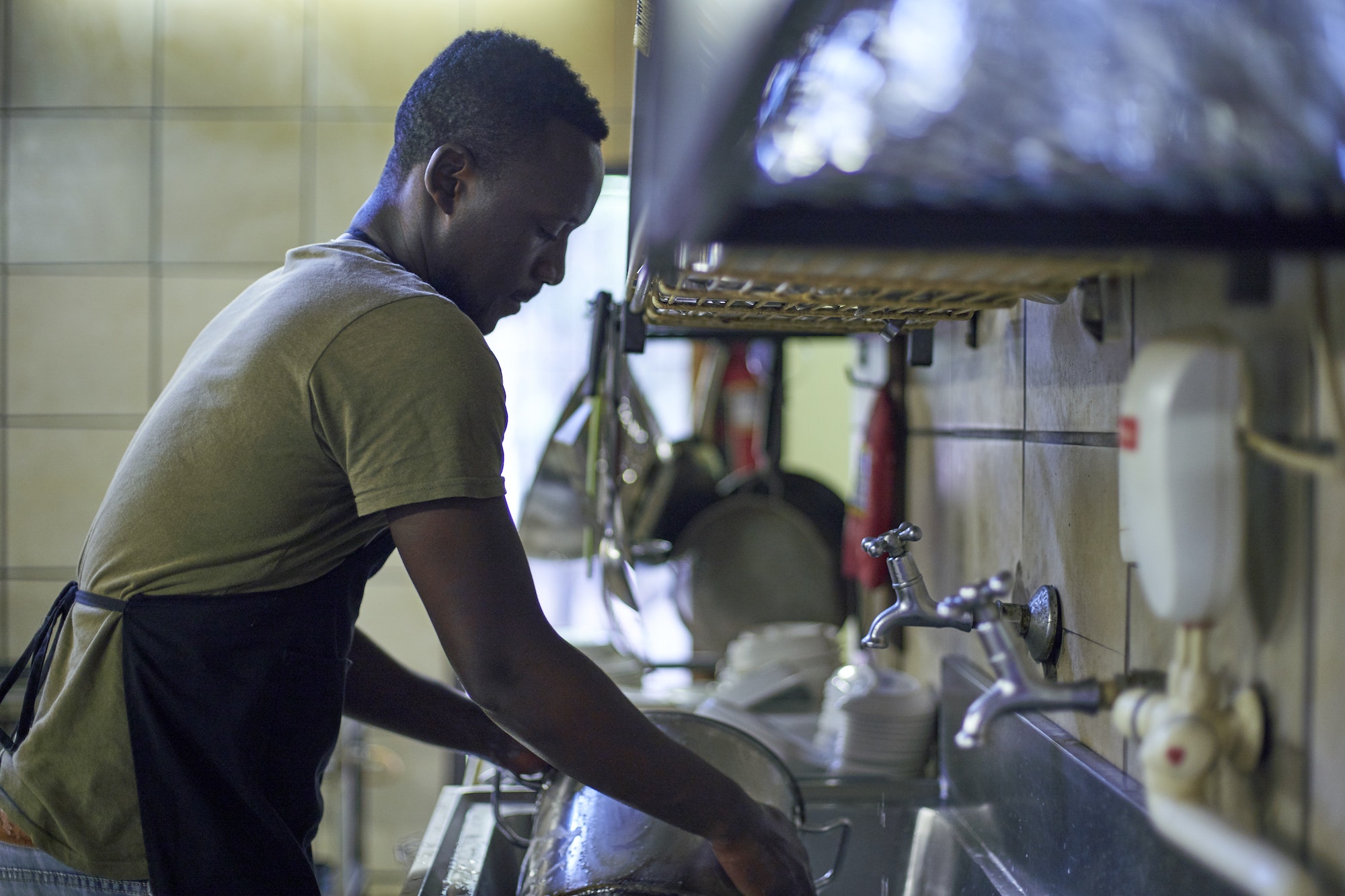 Young man washing dishes in restaurant kitchen, South Africa